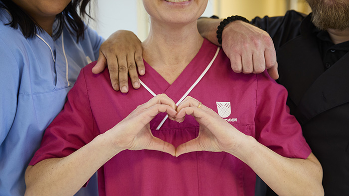 Närbild på tre personer i omvårdnadskläder, med händer som formar ett hjärta